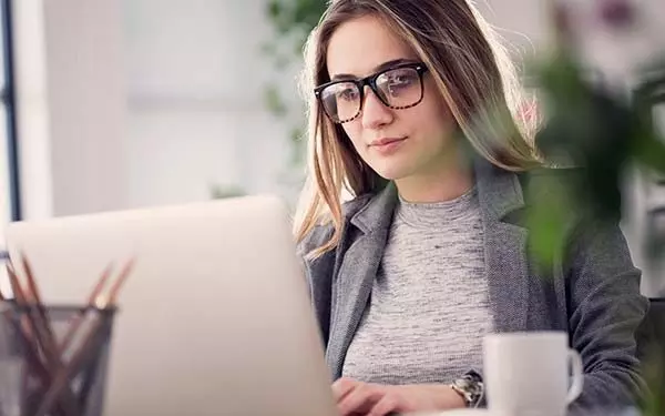 A blond woman wearing glasses working on a computer